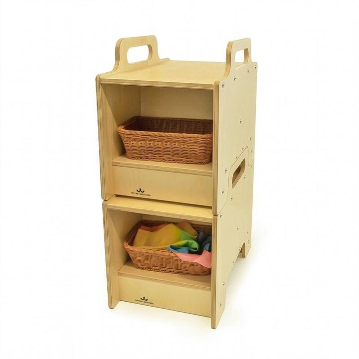 Two Whitney Brothers Stack-Able Seats stacked to form a two-sided storage cabinet with open compartments on both sides, each holding a wicker basket - showing the full flexible classroom storage and seating conversion in use