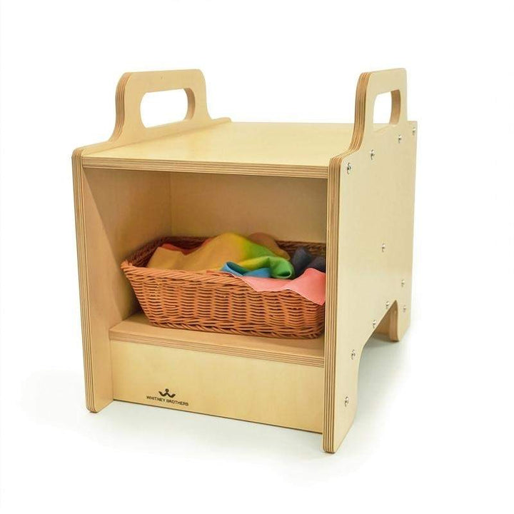 Whitney Brothers Stack-Able Seat with open storage compartment holding a wicker basket of colourful silk scarves, showing the accessible below-seat storage designed for early learning materials in daycare and classroom environments