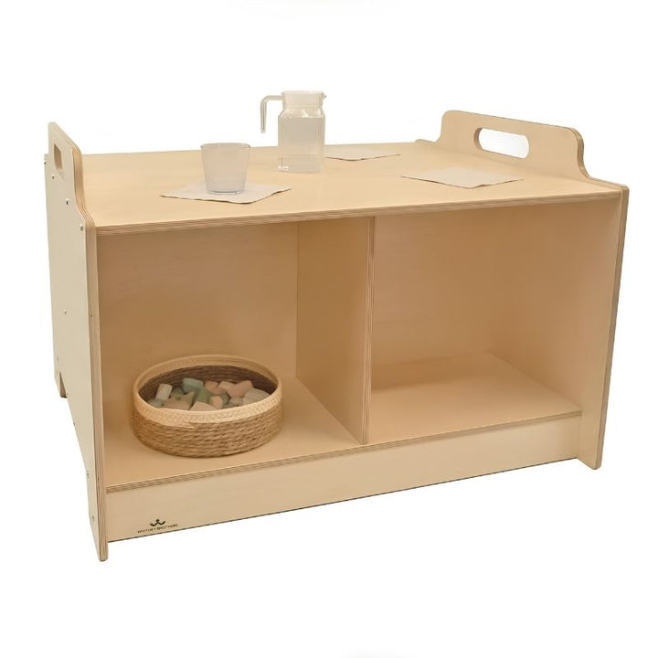 Whitney Brothers Stack-Able Table styled with Montessori practical life materials including a glass pitcher and drinking glasses on the surface, with manipulatives stored in the below-surface compartment