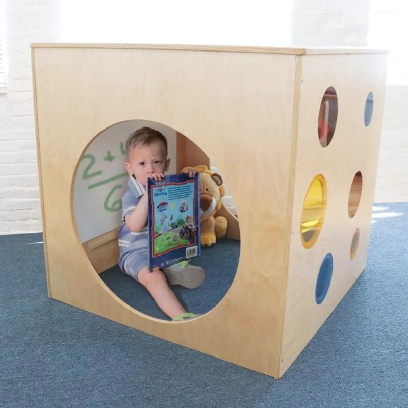Child playing with the Whitney Brothers Whitney Plus Porthole Play House Cube, showing the colourful red, yellow and blue acrylic portholes and tunnel side opening of the classroom quiet space cube