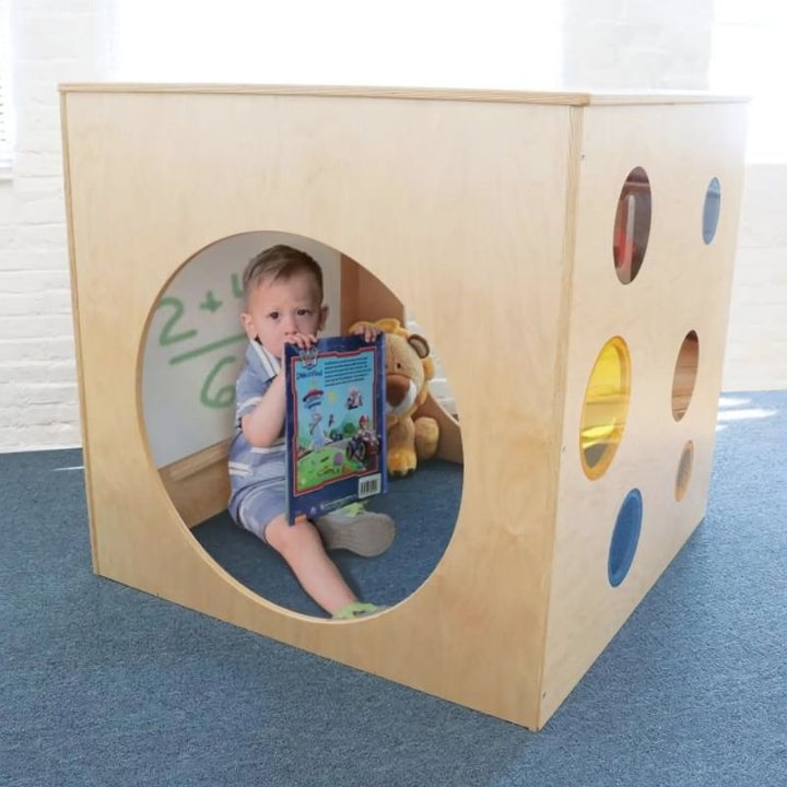 Child playing with the Whitney Brothers Whitney Plus Porthole Play House Cube, showing the colourful red, yellow and blue acrylic portholes and tunnel side opening of the classroom quiet space cube
